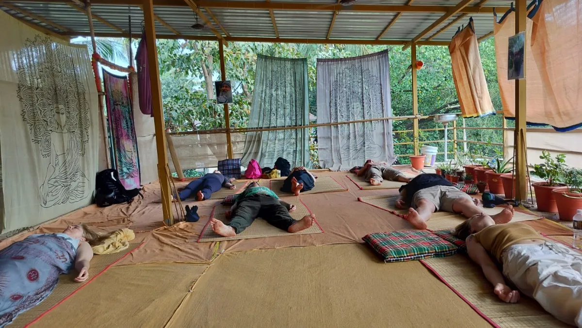 Students lying on mats in a shaded open-air meditation shala