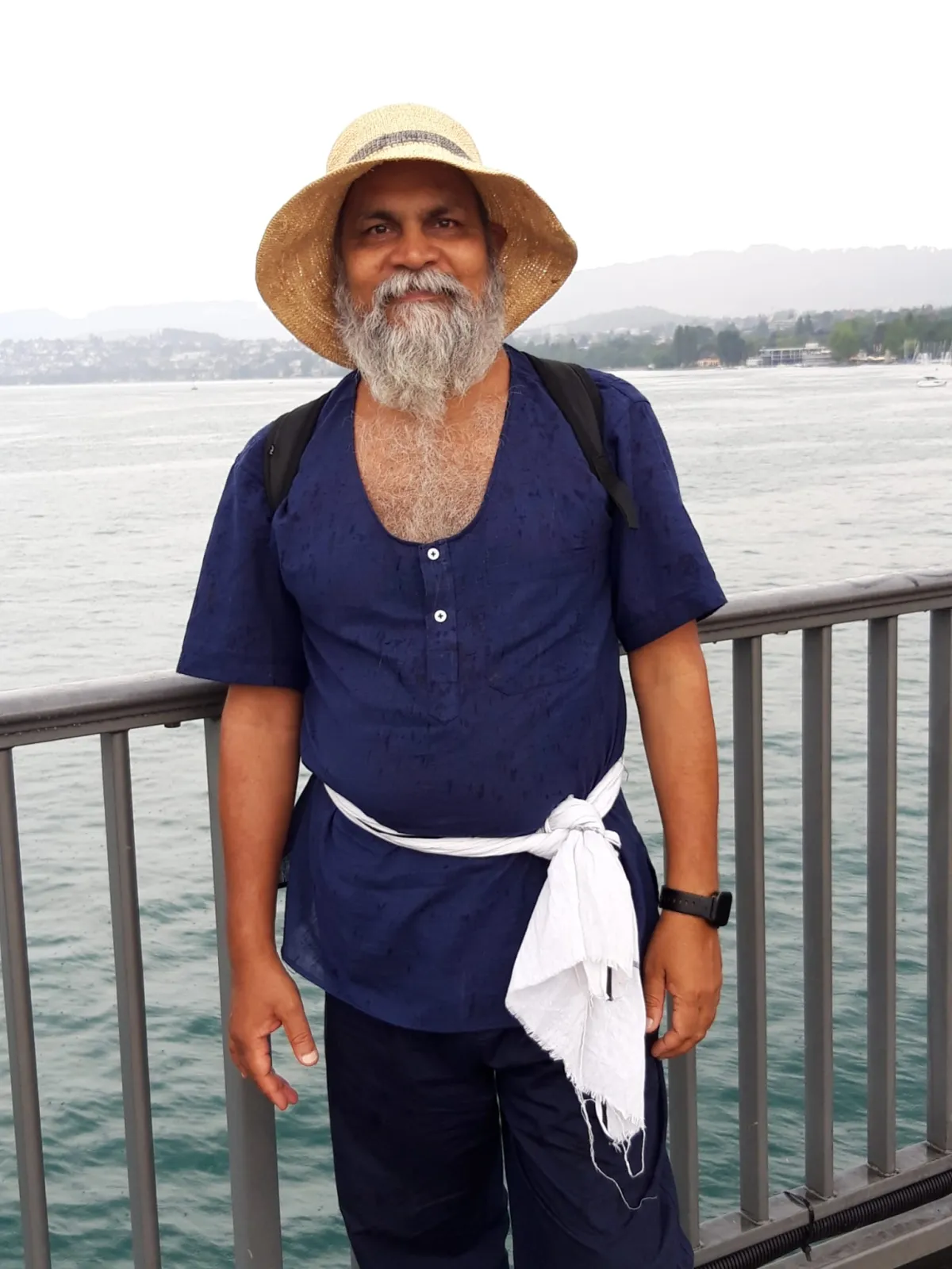 Swami Ashok Samdarshi in a straw hat on a bridge above a lake