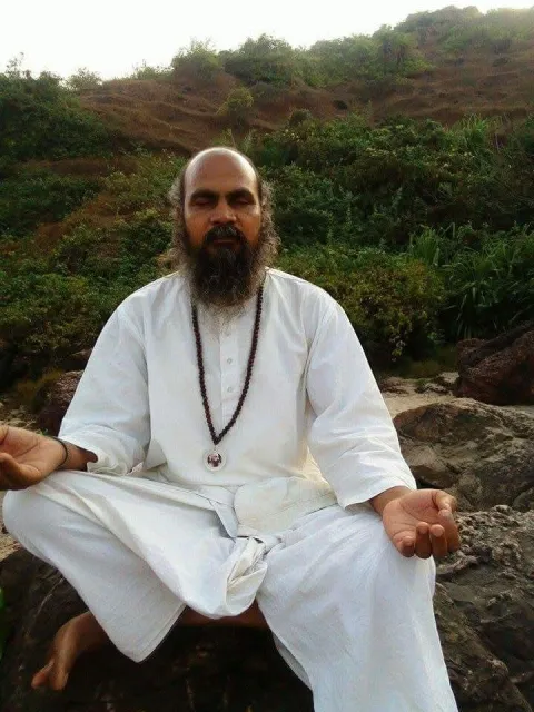 Swami-ji seated in meditation on a rock in green hills