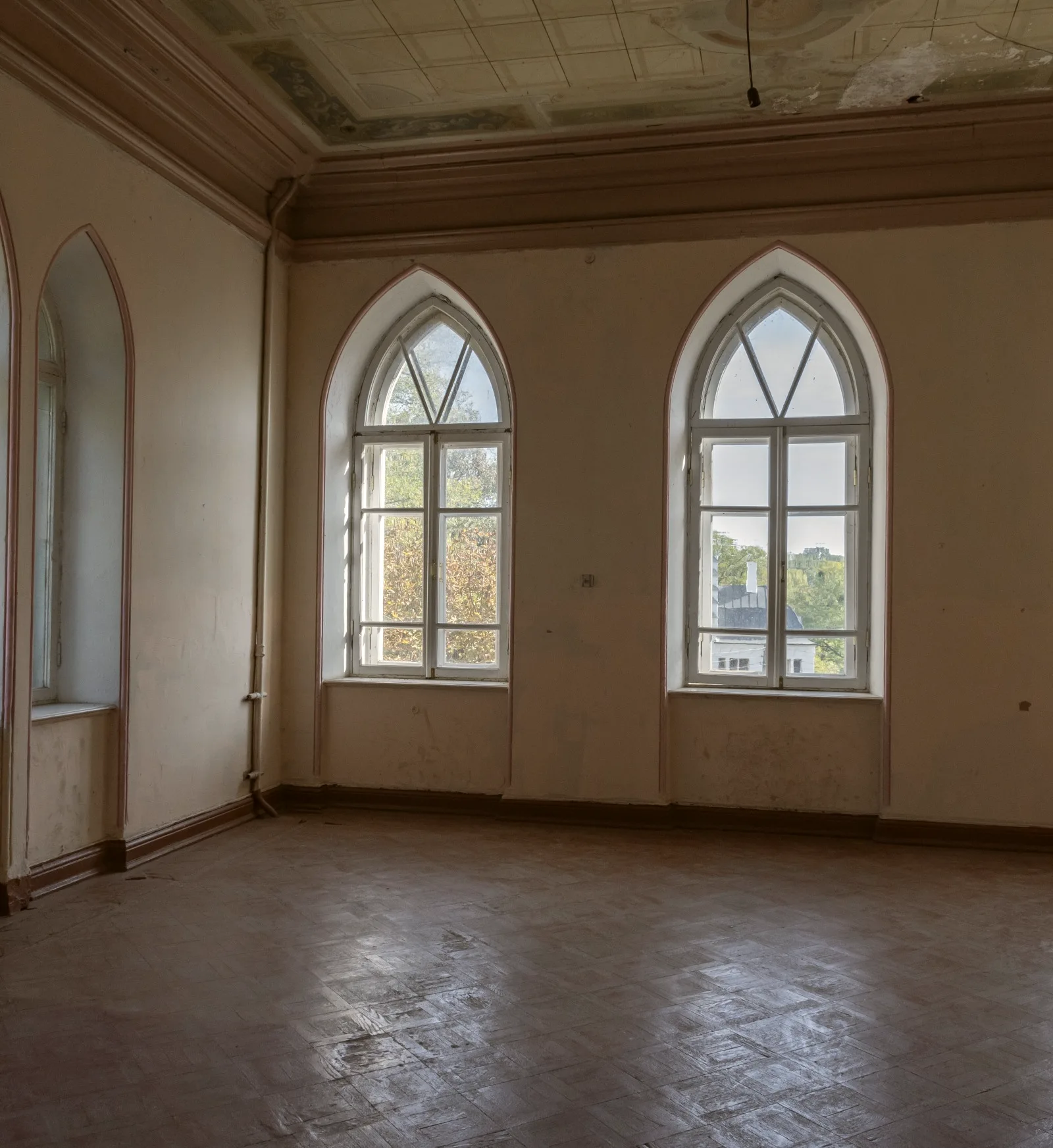 An empty room with tall arched windows and a bare wooden floor